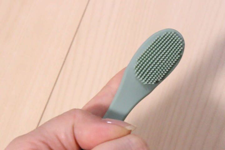 人差し指に薄い緑色のやわらかいペット用ブラシをはめている手元