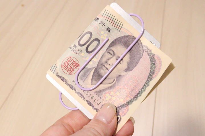 女性の指がパープルのビッグクリップでお札とカードを挟んでいる