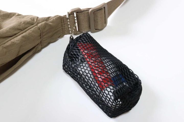 黒いメッシュポーチがベージュのバッグのベルトに付けられ、中にリップなどが見える