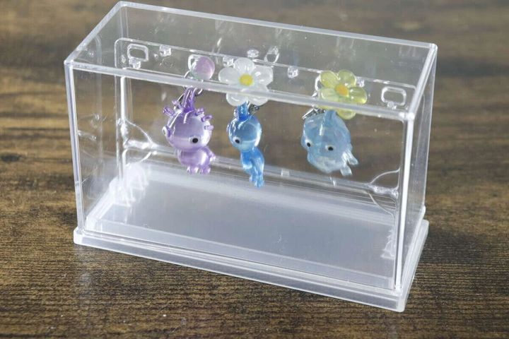 透明なミニチャームディスプレイケースの中に、3つの小さなチャームが吊るされている