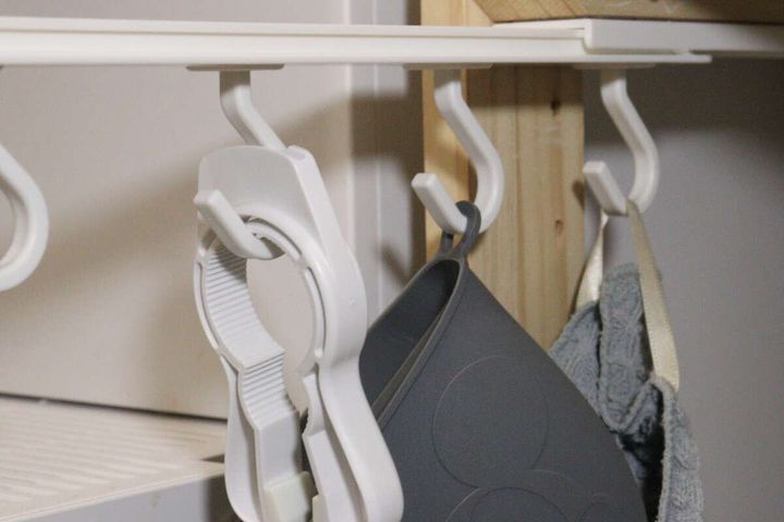 棚板下のフックに掛けられた鍋つかみやミトンが手前に引き出されている様子