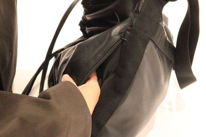 ブラックのドローストリングバッグのサイドファスナーを開ける手元