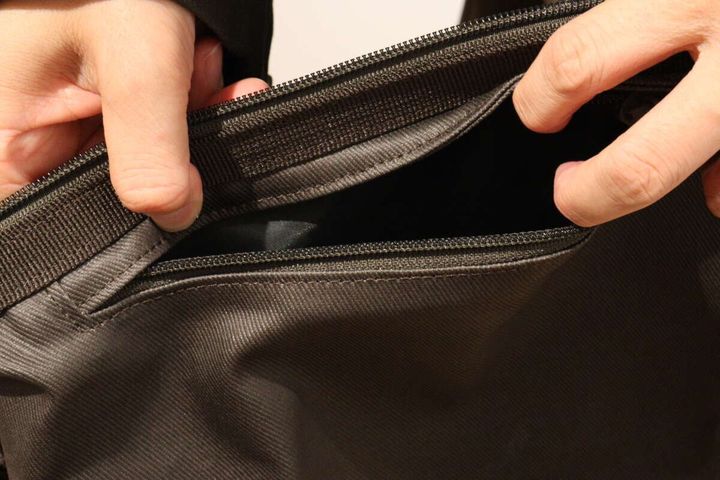 ダークブラウンのバッグの外側ポケットのファスナーを開ける手元