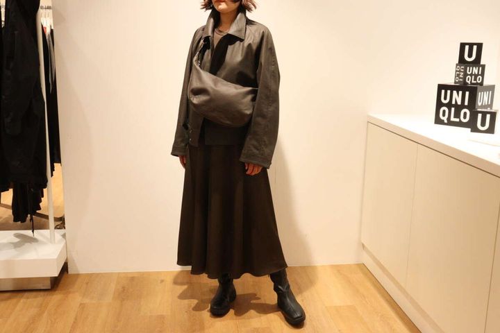 ダークブラウンのジャケットとスカートを着た女性がショルダーバッグを斜め掛け