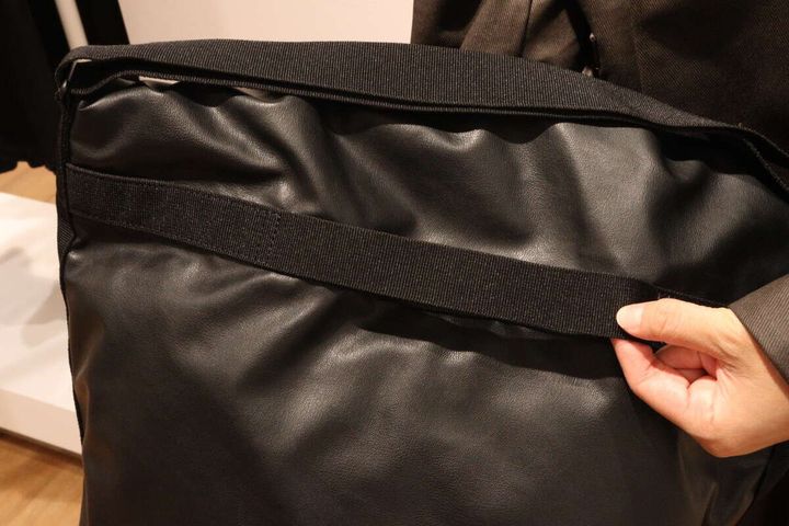 ブラックのドローストリングバッグ背面にあるテープループを指す手元