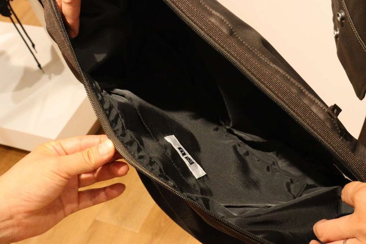 ダークブラウンのバッグのファスナーを開け内部を見せる手元