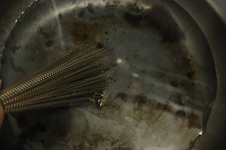 ステンレスブラシで汚れた中華鍋を洗っている