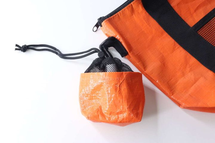 オレンジ色の大きなバッグの横に、同じくオレンジ色のマルチ巾着ポーチが吊り下げられている様子