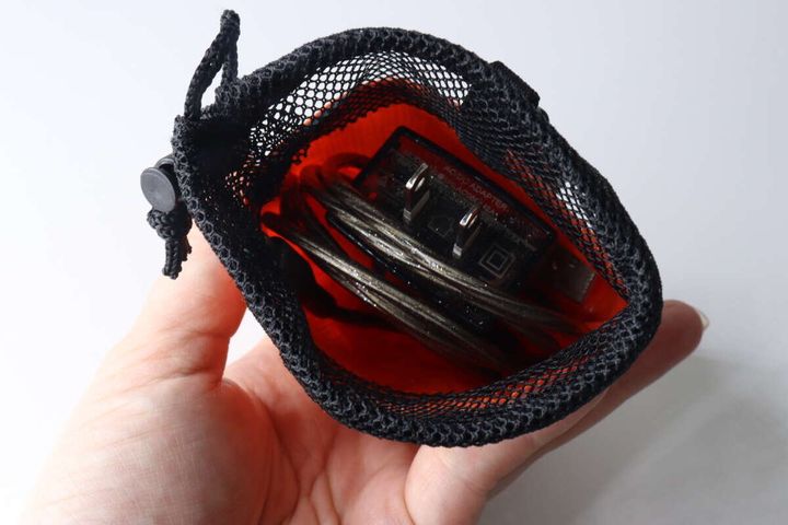 女性の手のひらに乗せたマルチ巾着ポーチの中に、充電ケーブルとアダプターが収納されている様子