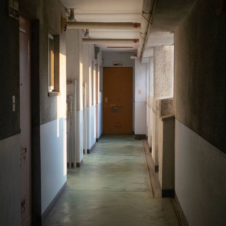 マンションの廊下。いくつか扉がある中に突き当りに黄色い扉。