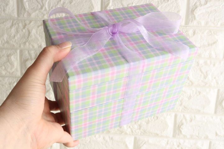 ラベンダー色のリボンでラッピングされたギフトボックスを持つ手