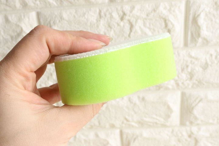 女性の手が緑色のキッチンスポンジの厚みがある側面を見せている