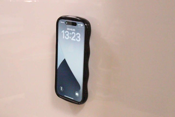 壁にシリコン携帯吸着マットで固定された黒いスマホ