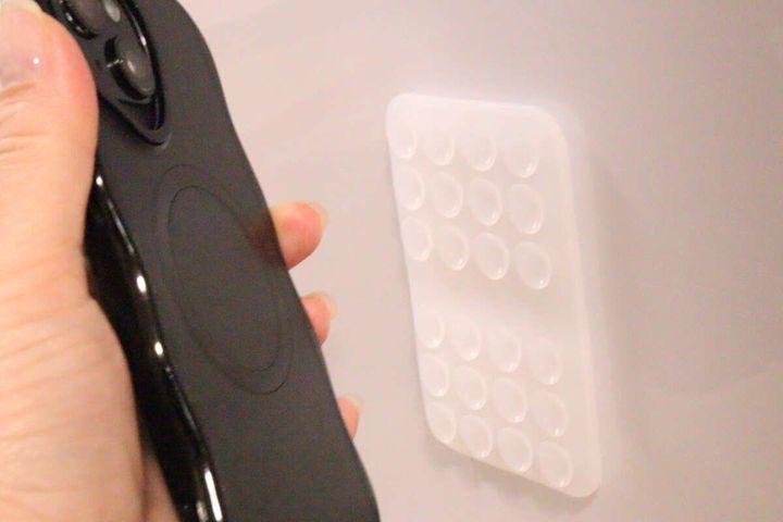 壁に貼られた吸着マットに黒いスマホを近づけている様子
