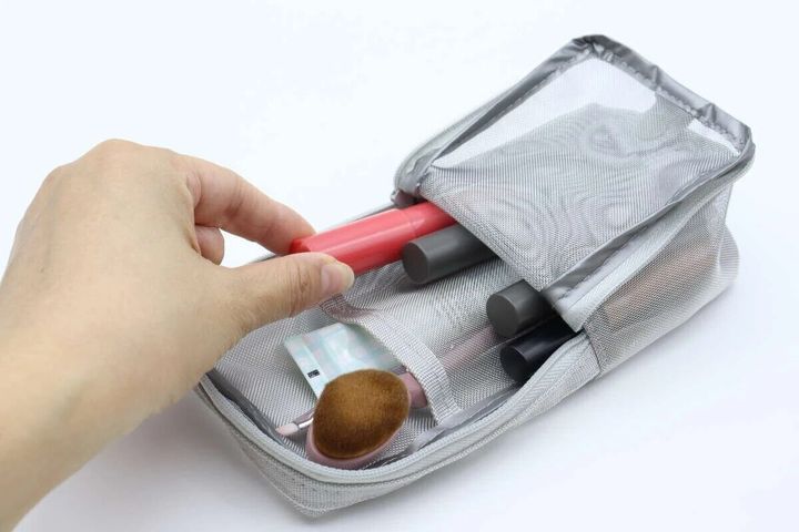 グレーのメッシュペンケースが開き、女性の手が赤いリップを取り出している