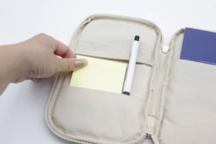 ベージュ色のペンケースが開き、女性の手が黄色い付箋を取り出している