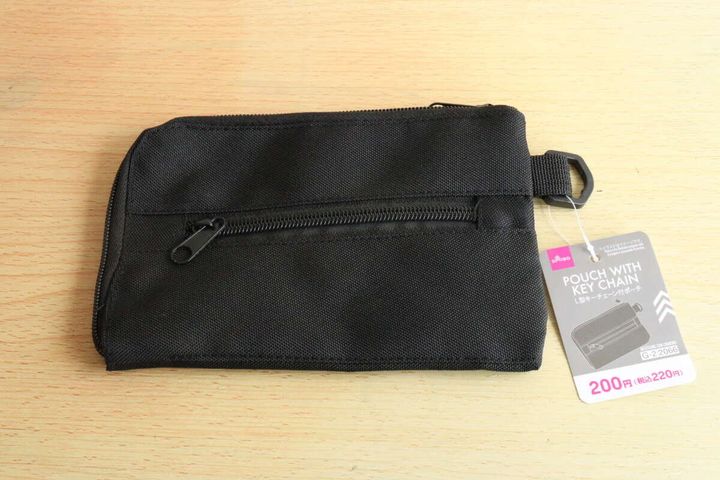 黒いL字型キーチェーン付ポーチが木目のテーブルに置かれ、値札が付いている