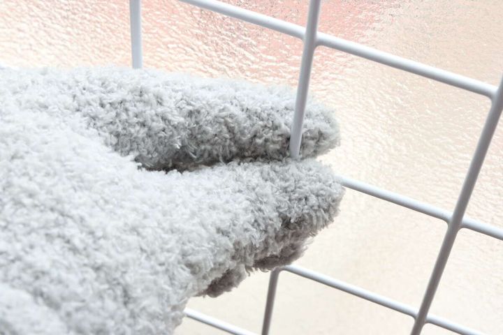 グレーのホコリ取り手袋で白い網状のラックの隙間を掴んで掃除している