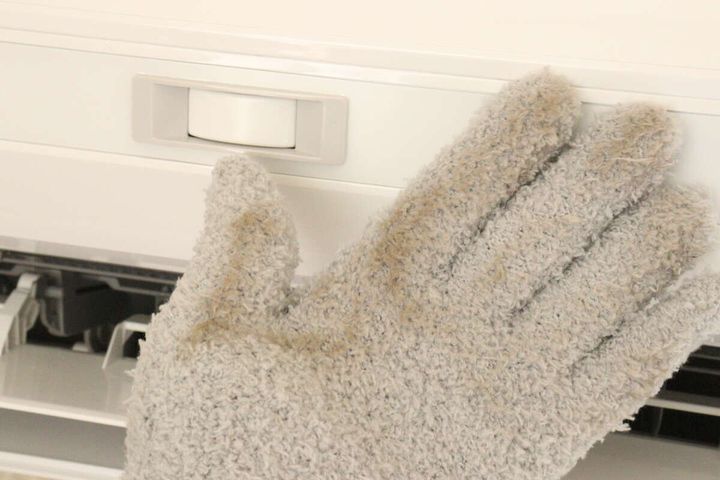 ホコリで汚れたグレーの手袋でエアコンの表面を拭いている
