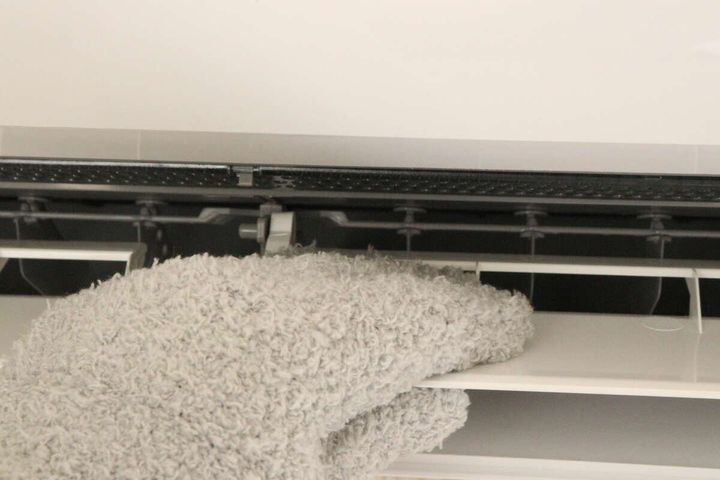 グレーのホコリ取り手袋でエアコンの吹き出し口の奥を拭いている
