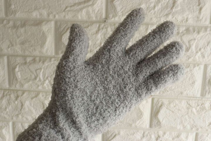 白いレンガ調の壁を背景に、グレーのホコリ取り手袋をはめた手のひら