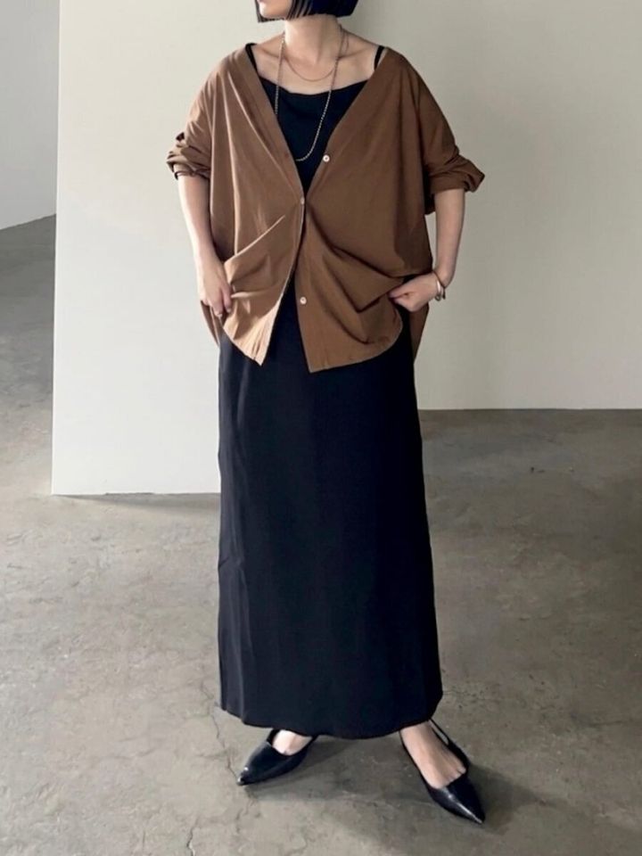 黒ワンピに茶色カーデを羽織り裾を少し持ち上げる女性