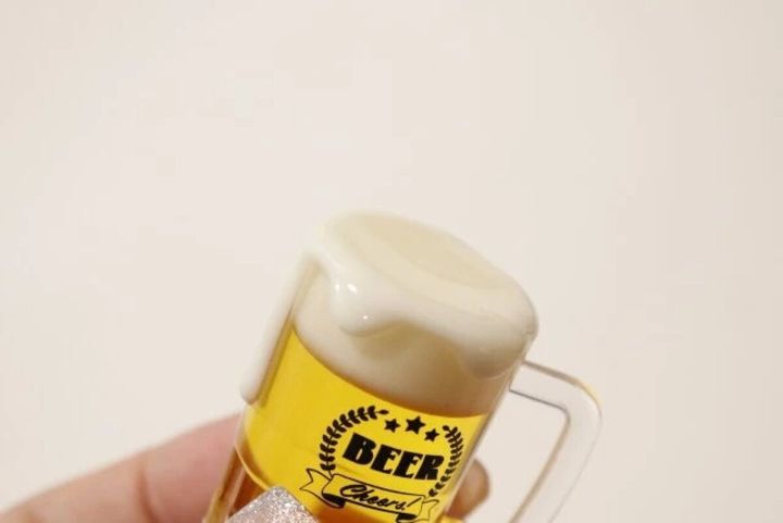 指で持たれたビールジョッキ型キーホルダーの泡のアップ