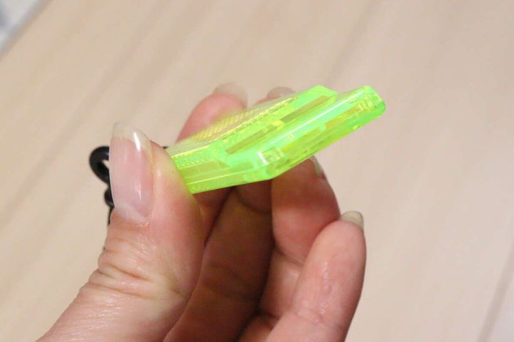 女性が反射材付きミニホイッスルを横から持ち、厚みを見せている