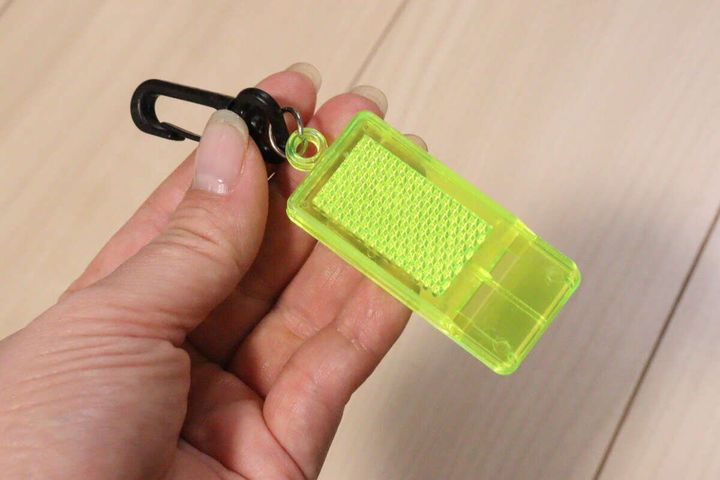 女性が蛍光イエローの反射材付きミニホイッスルを手に持っている
