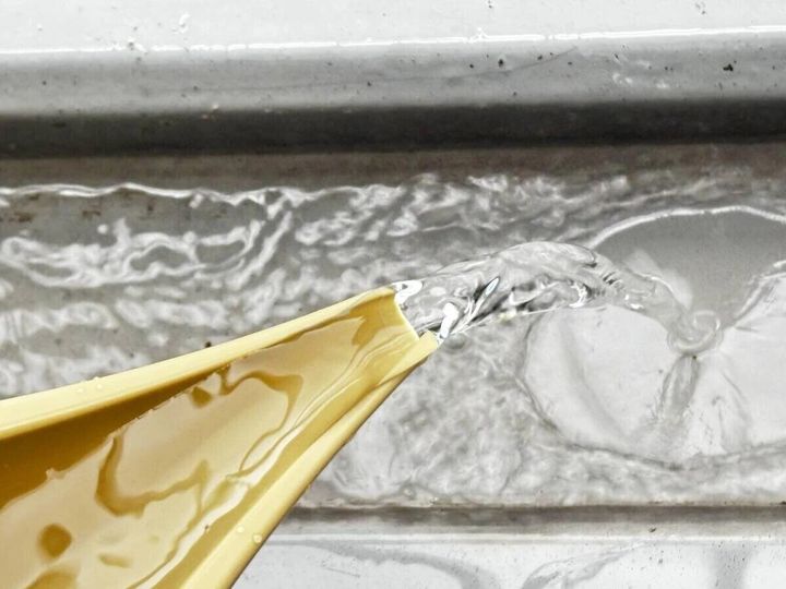 ベージュ色の水差しバケツのノズルから水が勢いよく流れ出ている