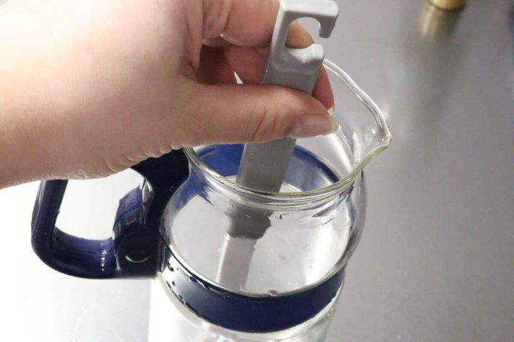 女性がダイソーのボトル洗いブラシをガラスポットの口から出し入れしている