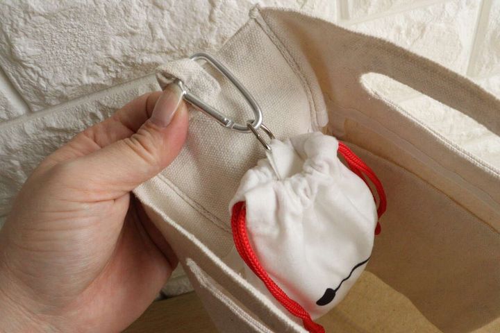 女性の手が白い巾着袋をカラビナでトートバッグに吊り下げている