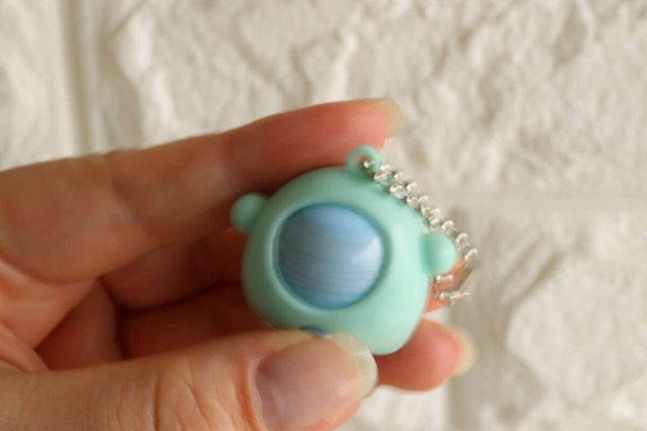 女性の指が水色のじゃんけんキーホルダーを持ち絵柄が回転中