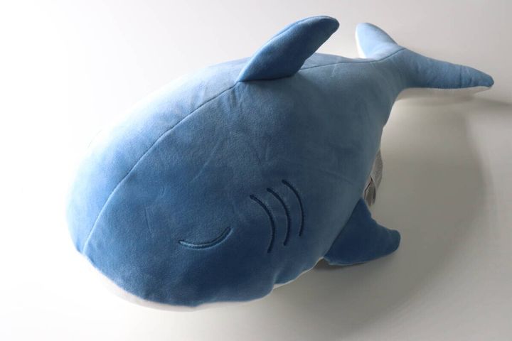 白い背景に置かれた、眠る表情の青いサメクッション
