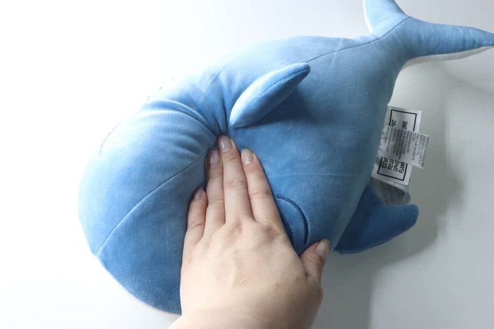 女性の手が青いサメクッションを押し、もちふわ感を確かめる
