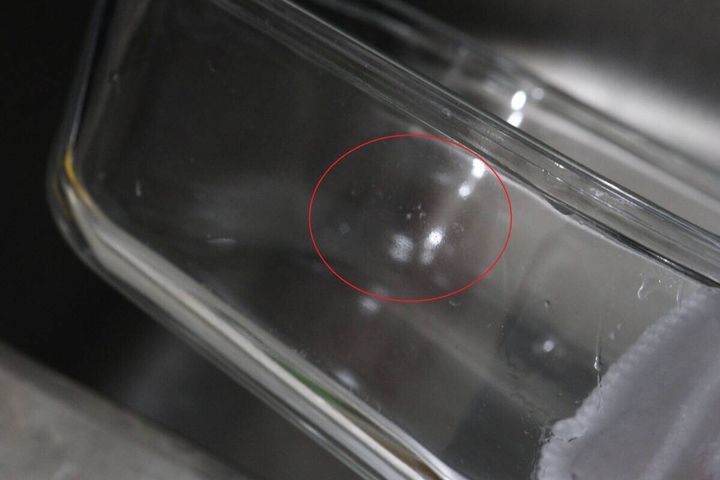 ガラス容器の底にこびりついた白い汚れを赤丸で囲んで示している