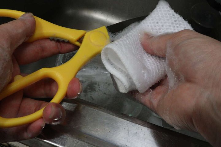 黄色いキッチンばさみをメッシュクロスで洗っている手元