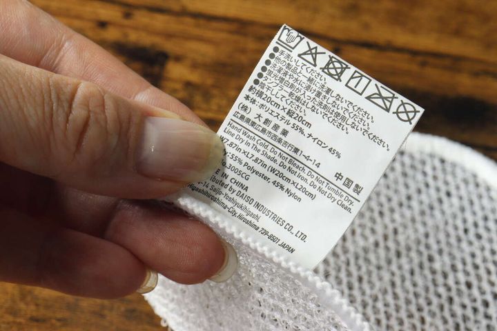 手で持ったメッシュクロスのタグに記載された洗濯表示と注意書き