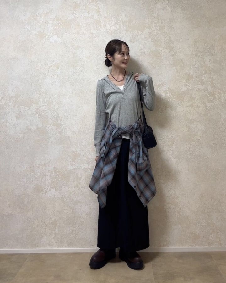 グレーのフーデッドリブTシャツにチェックシャツを腰巻きした女性