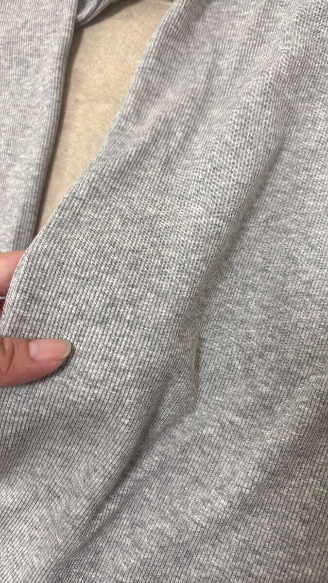 指でつまんで見せているグレーのフーデッドリブTシャツの生地アップ