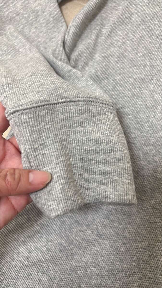 指でつまんで見せているグレーのフーデッドリブTシャツの袖口アップ