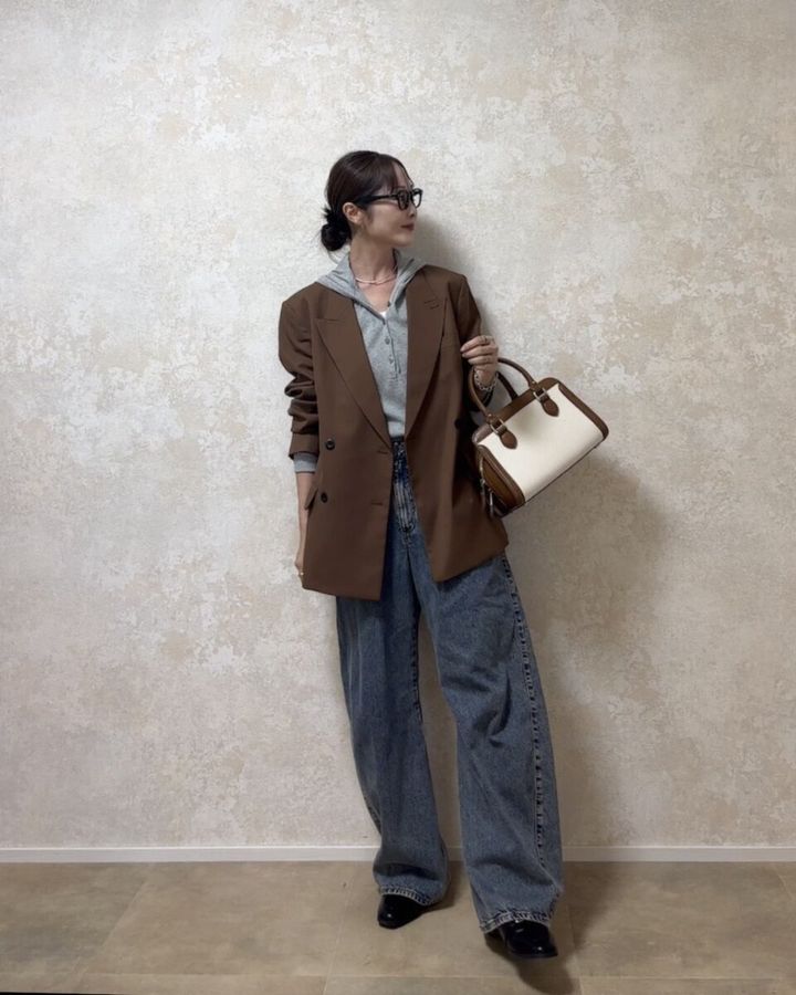 グレーのフーデッドリブTシャツに茶色ジャケットとデニムを着用した女性
