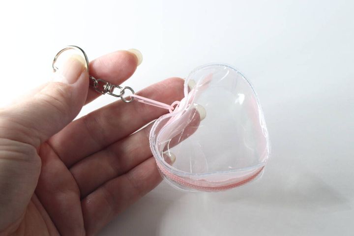 女性の指がハート形のクリアポーチのキーホルダー部分を持っている様子
