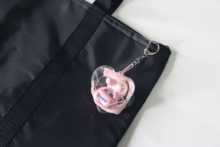 黒いバッグのファスナー部分に、ハート形ポーチがキーホルダーとして付けられている様子