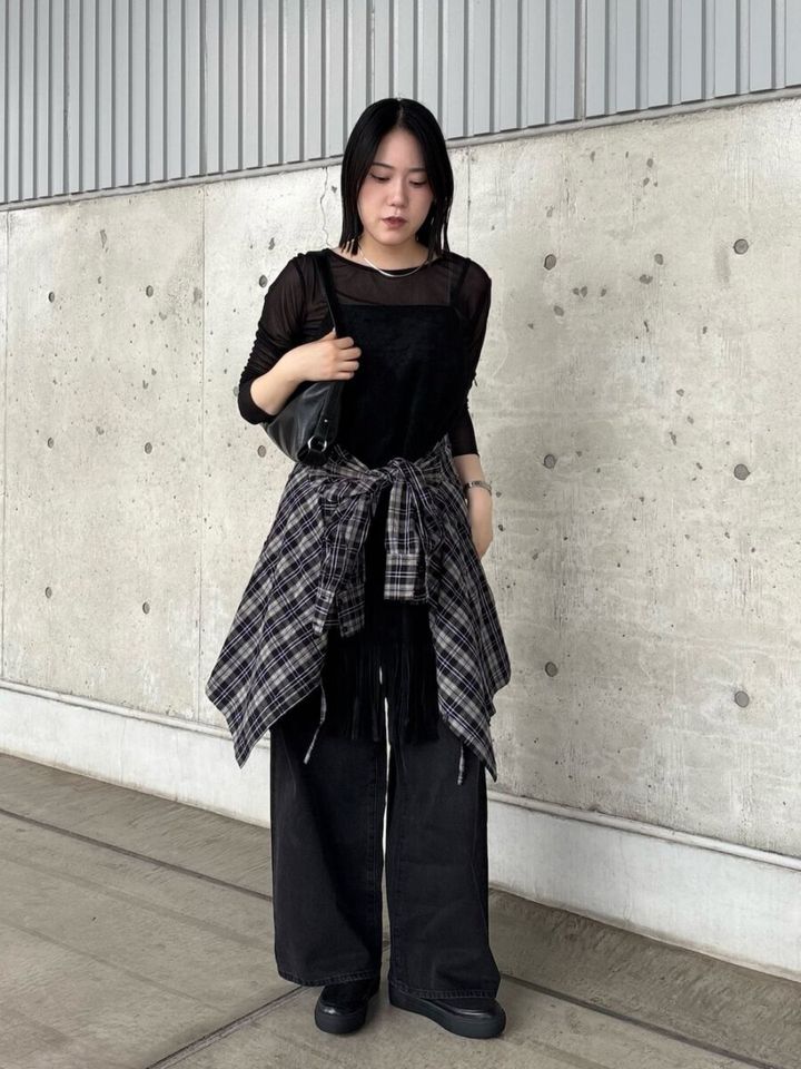 黒のシアートップスとワイドパンツにチェックシャツを腰巻きした女性が立っている