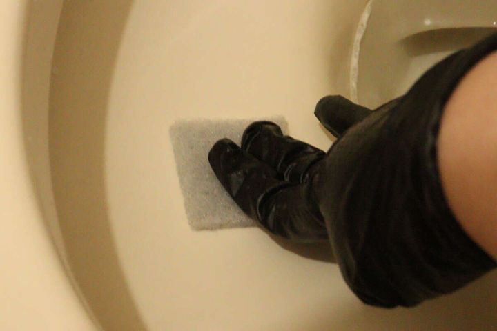 黒い手袋をはめた手がトイレの便器内をスポンジでこする