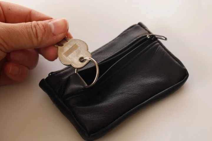 男性が黒い本革小銭入れのキーリングに鍵をつけようとしている
