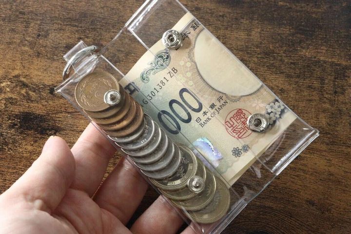 手が透明なPVCコインポーチを持ち、中に硬貨と千円札が入っている