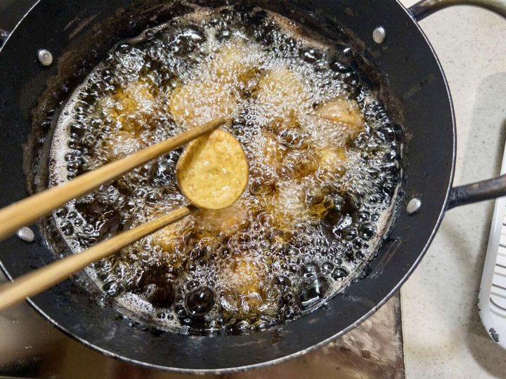 黒いフライパンで熱い油で揚げられているじゃがいも。箸で一つ持ち上げられている。