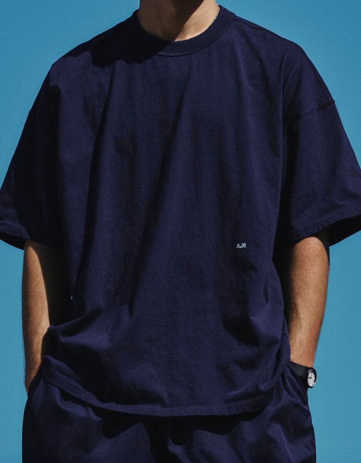 コンビニエンスウェアを代表する無地のアウターTシャツを、「A.H」らしいビッグシルエットで表現した男女兼用モデル。前身頃には「A.H」のロゴを小さく配置。しろとネイビーの2色を用意し、XXL相当のワンサイズで展開している。